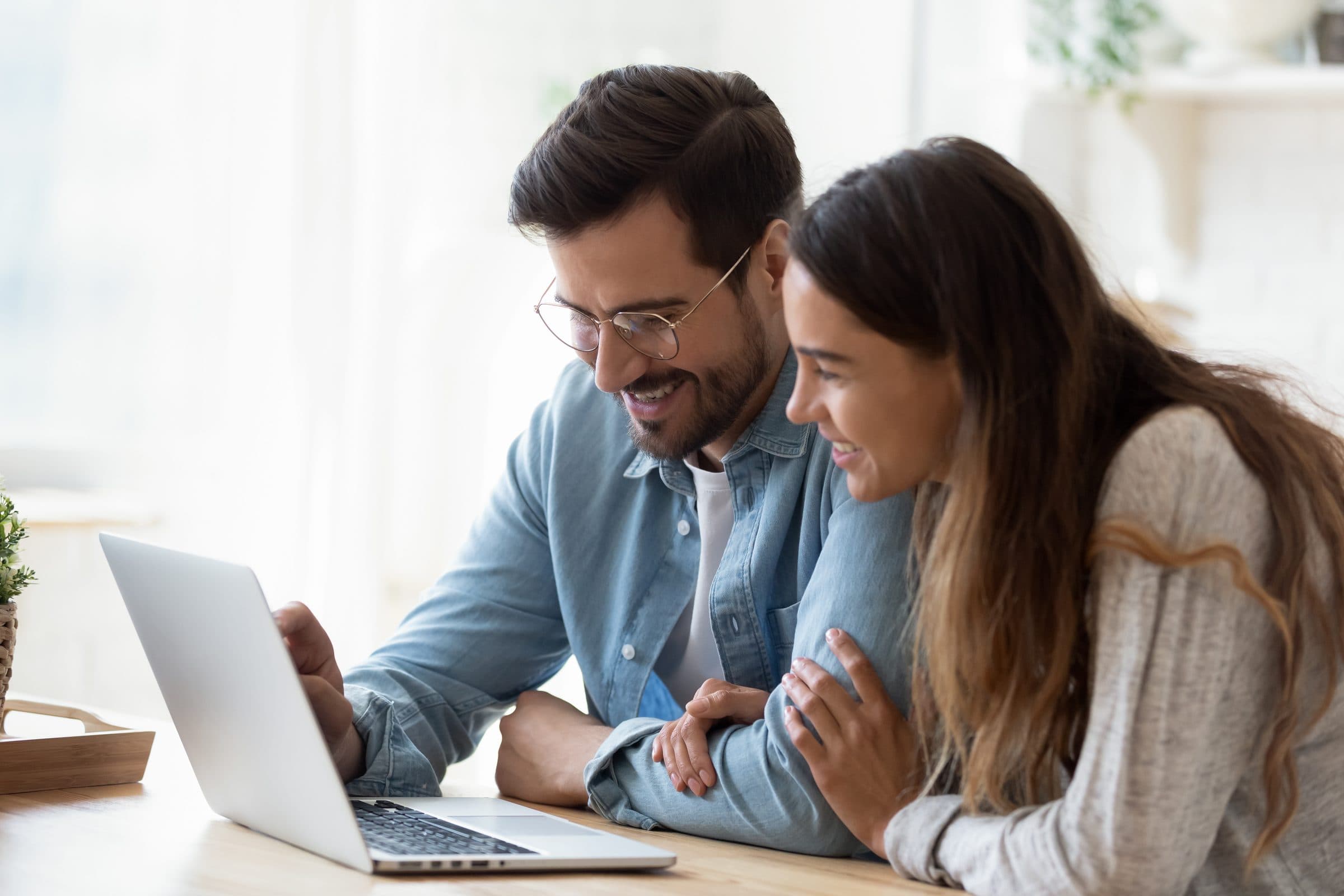 A couple at a table smiling at a laptop together